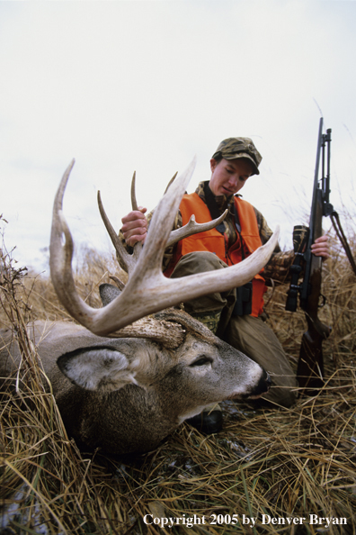 Young hunter with bagged white tail deer in a field.