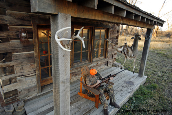 Hunter on porch of cabin checking out rifle.