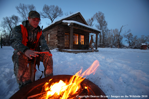 White-tailed deer hunter warming hands by campfire.