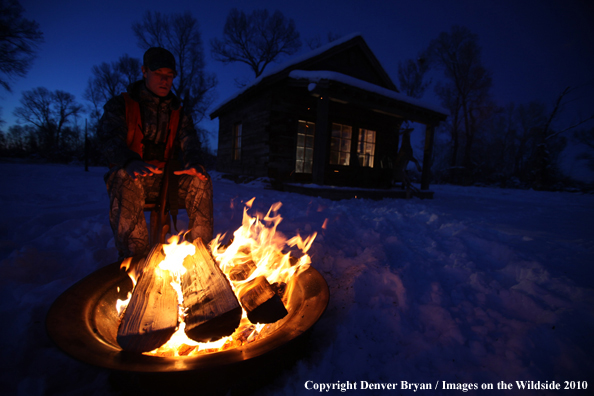 White-tailed deer hunter warming hands by campfire.