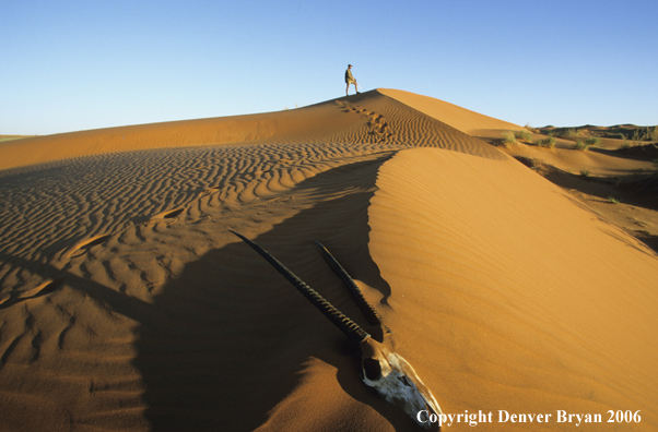 African hunter standing atop sanddune.