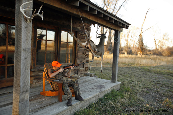 Hunter sitting on old cabin porch checking rifle.