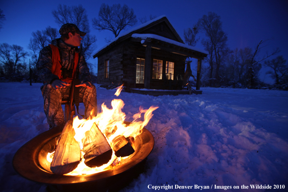 White-tailed deer hunter warming hands by campfire.
