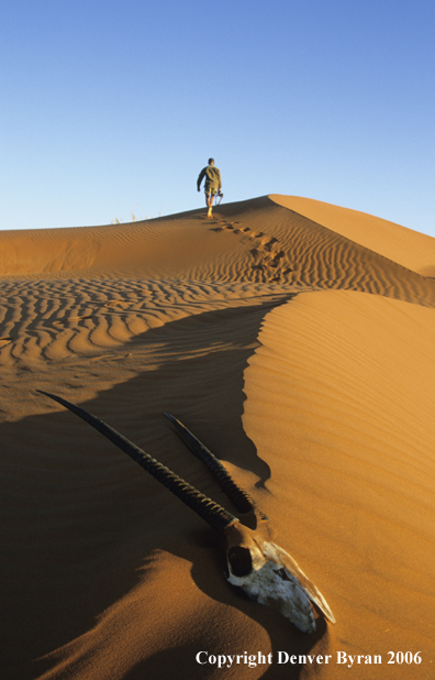 African hunter walking along sanddunes.