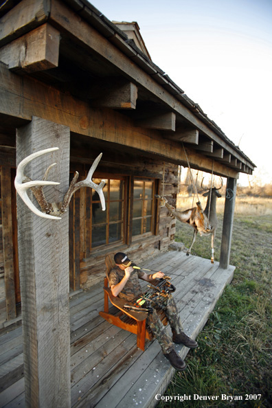 Archery hunter sittting on porch of old hunting shack where bagged white-tail hangs