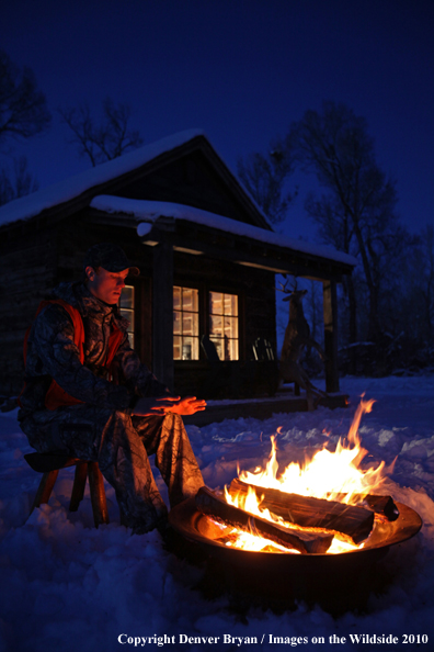 White-tailed deer hunter warming hands by campfire.