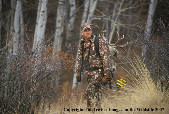 Bowhunter in field packing out caped mule deer on back.