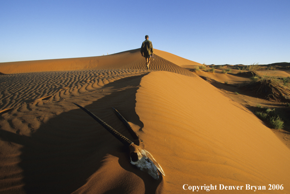African hunter walking atop sanddune.