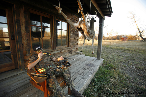 Archery hunter sittting on porch of old hunting shack where bagged white-tail hangs