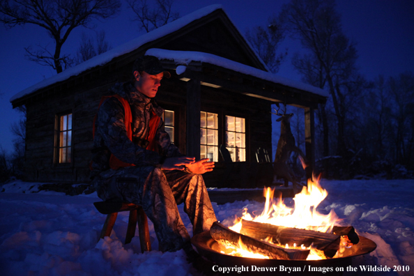 White-tailed deer hunter warming hands by campfire.