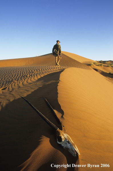 African hunter walking atop sanddunes.