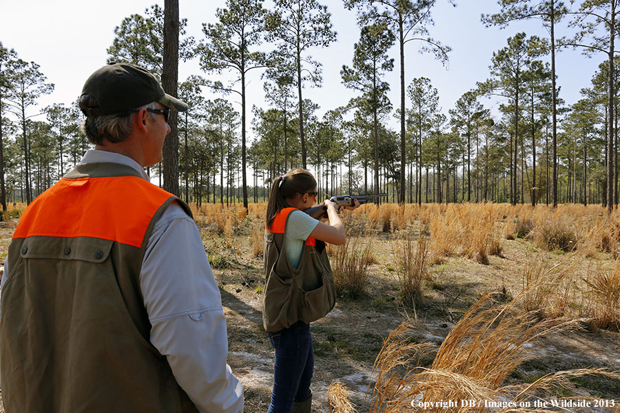 Adult with young hunter in field.