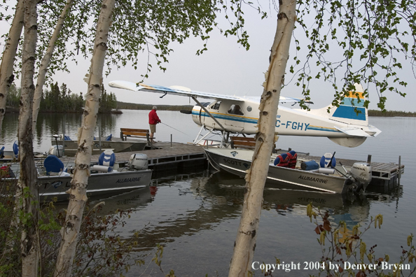 Fisherman flyfishing from the dock with float plane and fishing boats tied up nearby.  Saskatchewan.