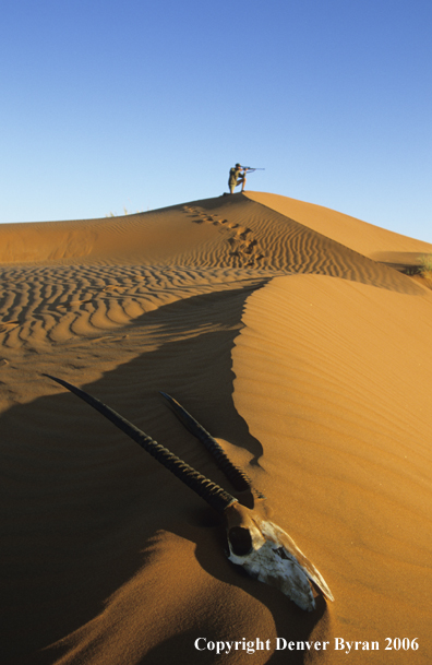 African hunter shooting atop a sanddune.