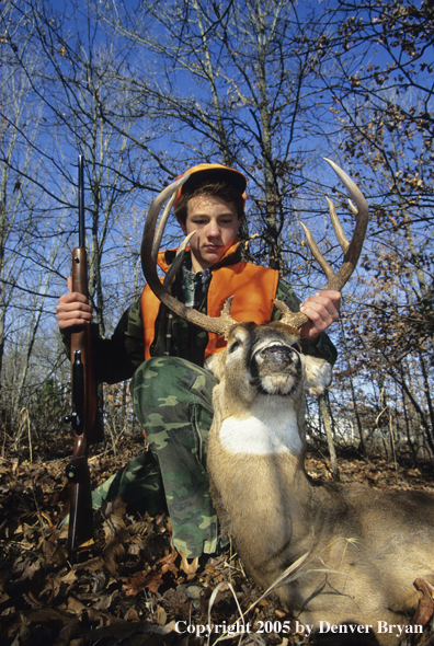 Young hunter with whitetail deer in woods.