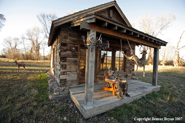 Archery hunter sittting on porch of old hunting shack where bagged white-tail hangs