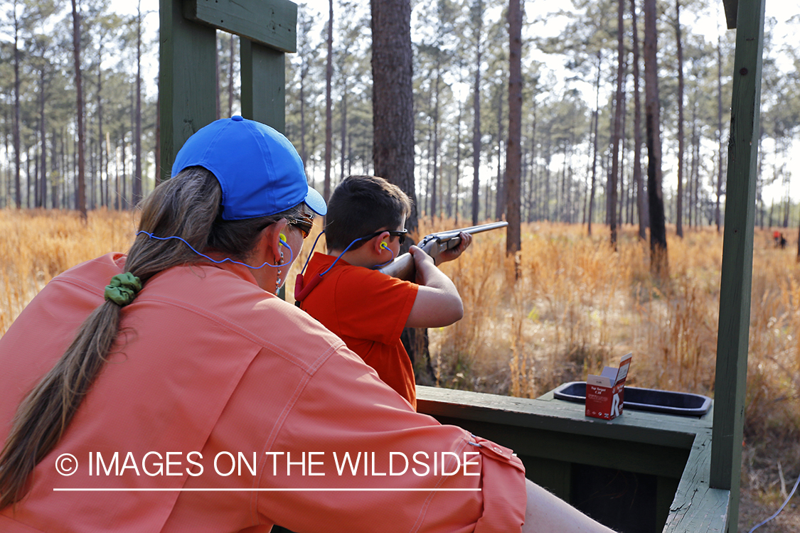 Adult with young hunter in field.
