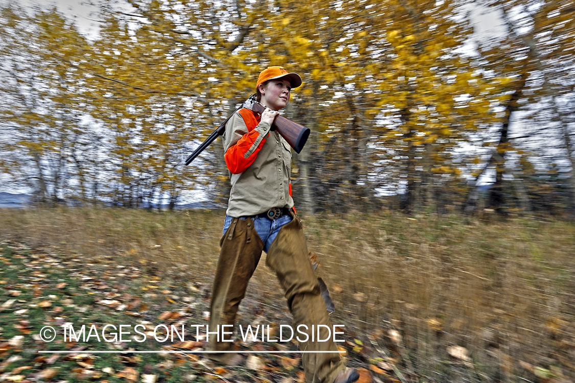 Woman with bagged pheasant walking field line.