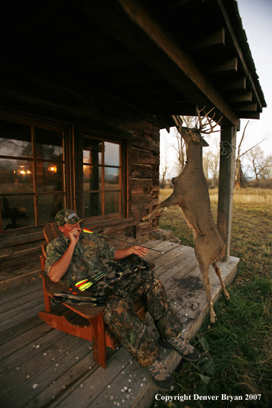 Archery hunter sittting on porch of old hunting shack where bagged white-tail hangs