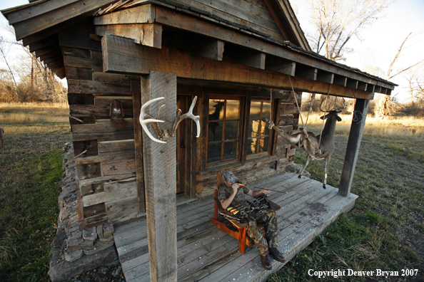 Archery hunter sittting on porch of old hunting shack where bagged white-tail hangs