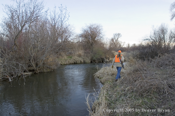 Woman big game hunter walking along river.