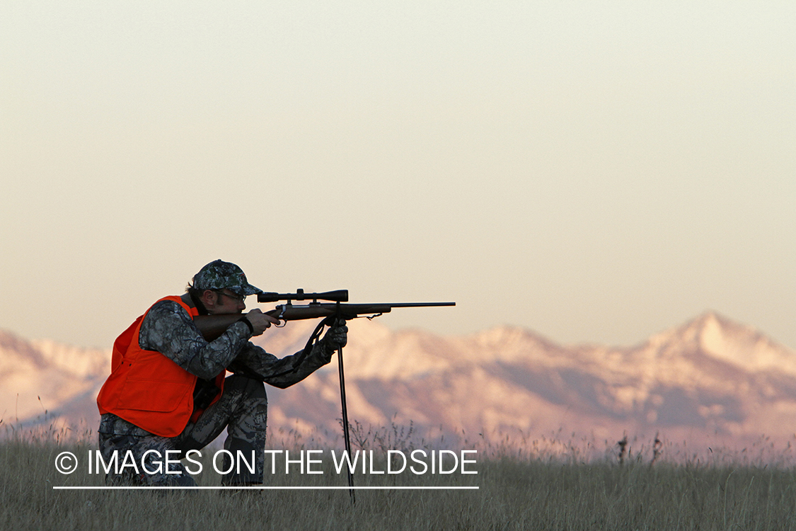 Big game hunter taking aim in field. 