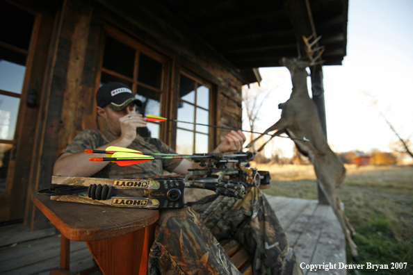 Archery hunter sittting on porch of old hunting shack where bagged white-tail hangs