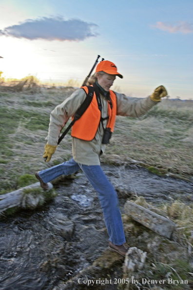 Woman big game hunter crossing small creek.