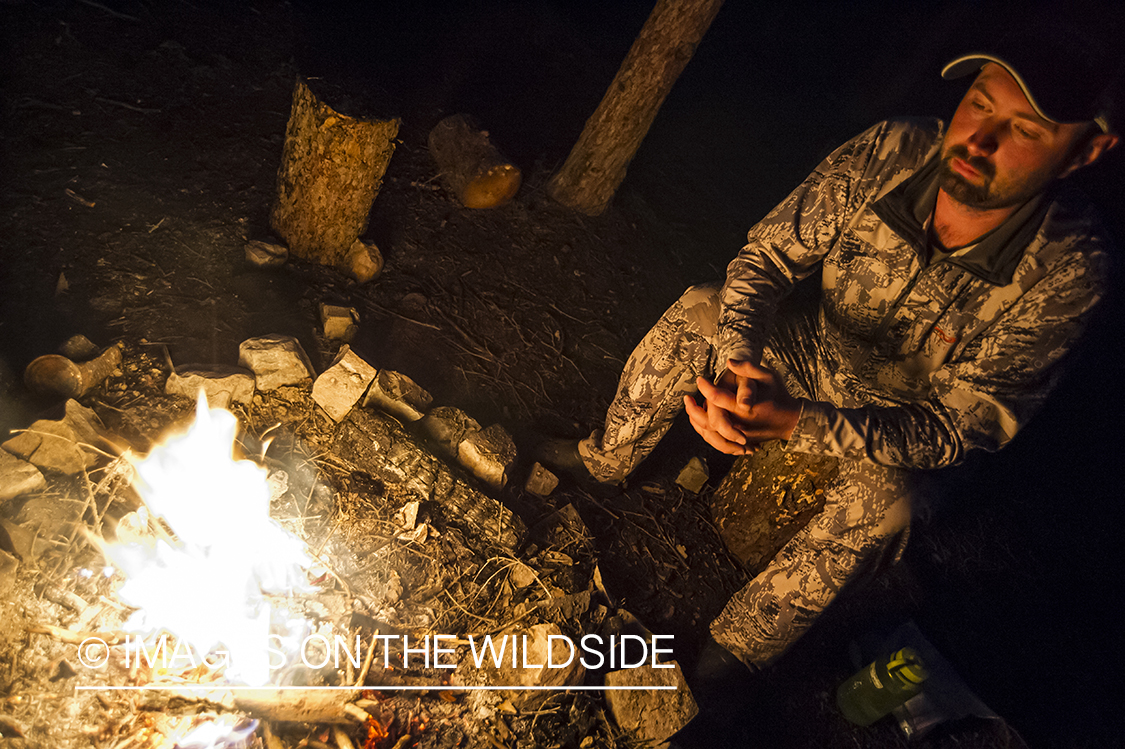 Hunter sitting by campfire at night.