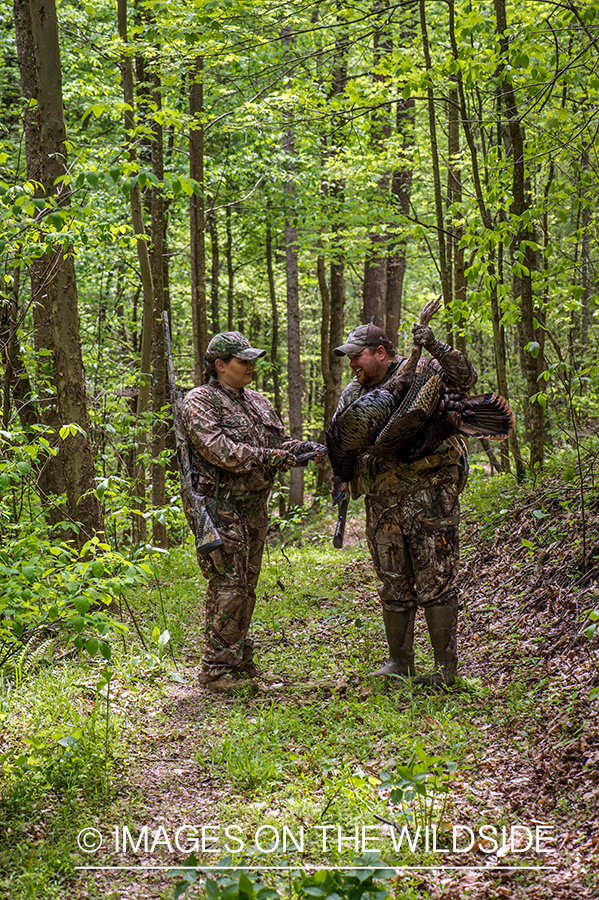 Man and woman turkey hunters in field with turkey.