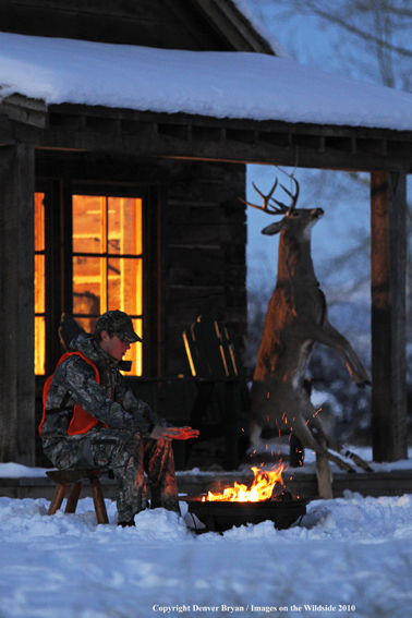 White-tailed deer hunter warming hands by campfire