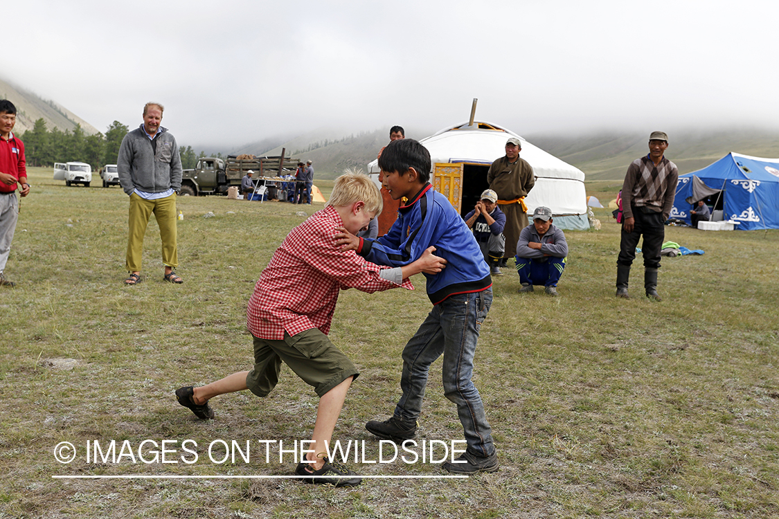 Mongolian and American boys wrestling in fishing camp.