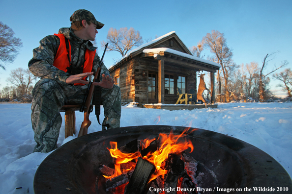 White-tailed deer hunter warming hands by campfire