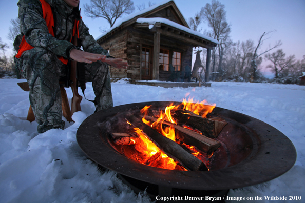 White-tailed deer hunter warming hands by campfire