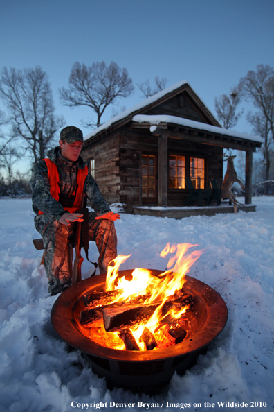 White-tailed deer hunter warming hands by campfire