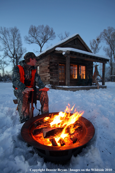 White-tailed deer hunter warming hands by campfire