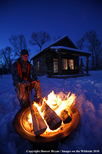 White-tailed deer hunter warming hands by campfire