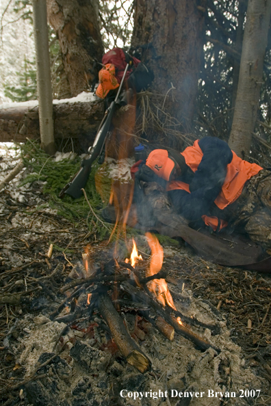 Elk hunter sleeping around campfire in woods.