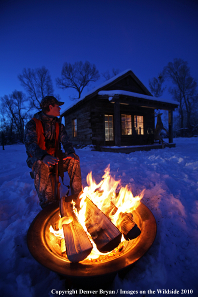 White-tailed deer hunter warming hands by campfire