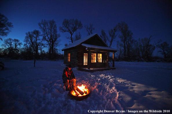 White-tailed deer hunter warming hands by campfire