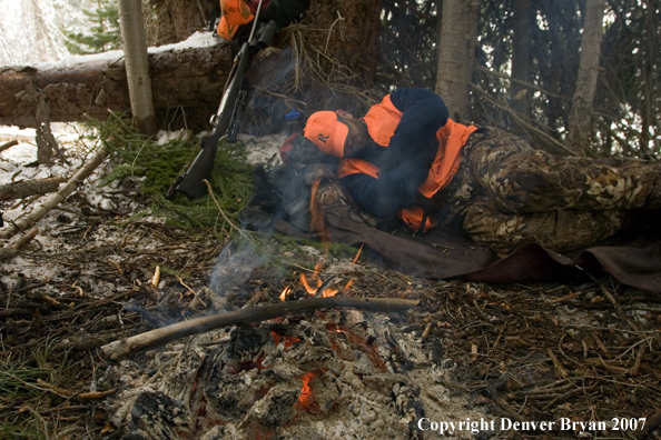Elk hunter sleeping around campfire in woods.