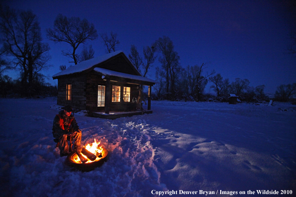 White-tailed deer hunter warming hands by campfire