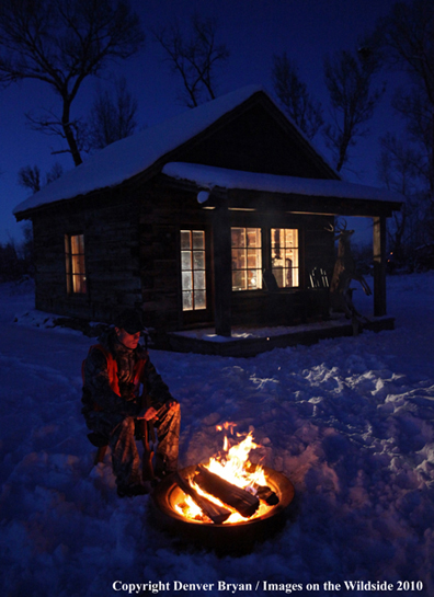 White-tailed deer hunter warming hands by campfire