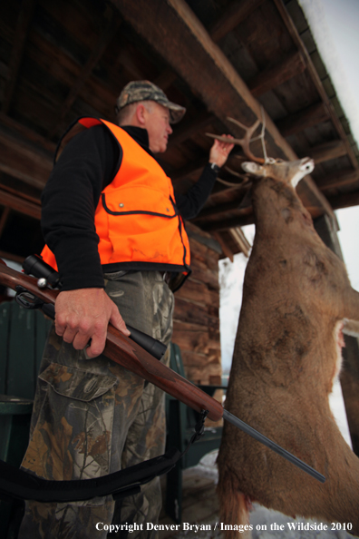 White-tailed deer hunter stands with buck hanging from cabin.