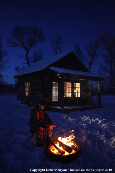 White-tailed deer hunter warming hands by campfire