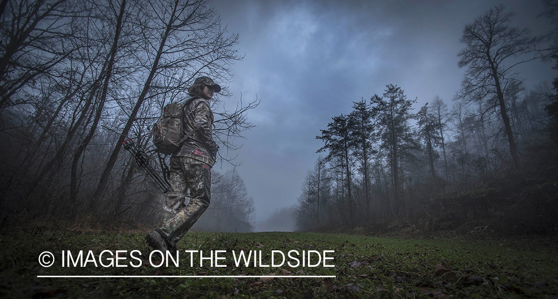 Woman bowhunting in fall forest.