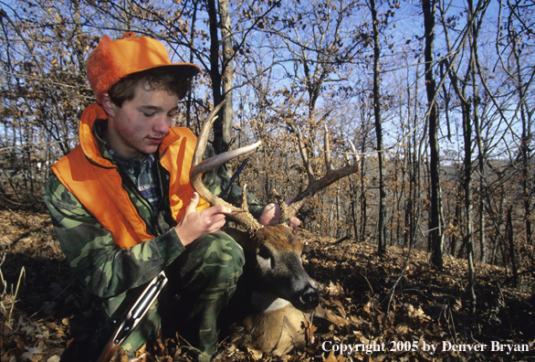 Young hunter with whitetail deer in the woods.