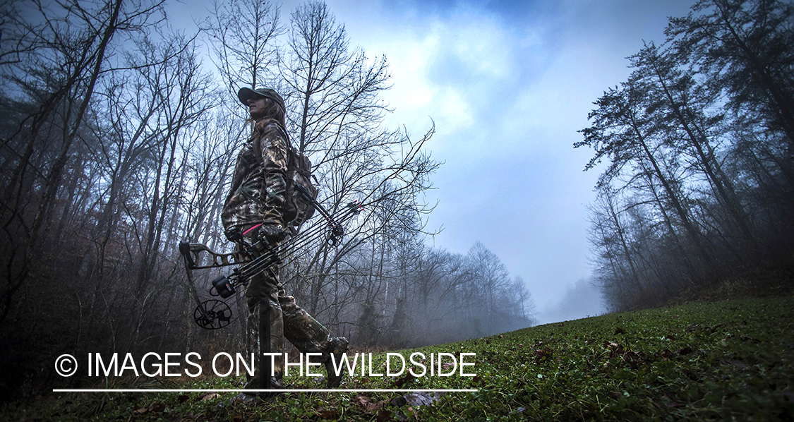 Woman bowhunting in fall forest.
