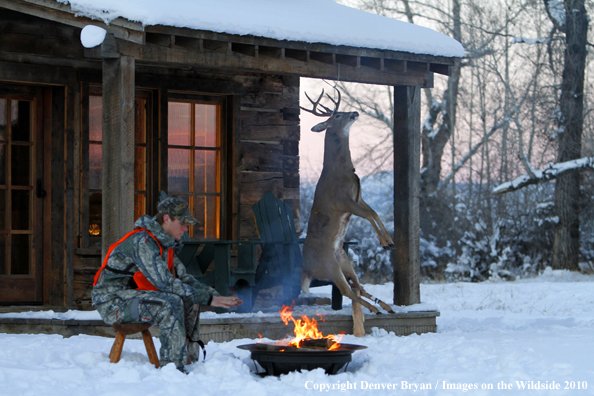 White-tailed deer hunter warming hands by campfire.