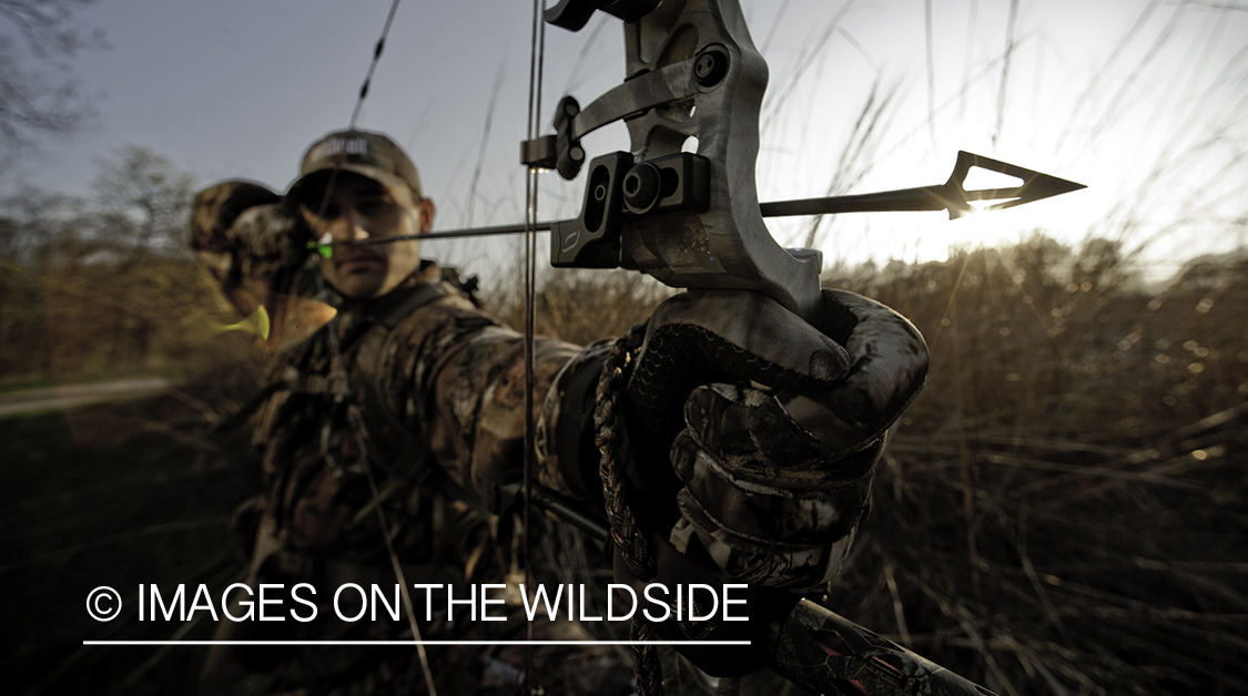 Bowhunter taking aim in field. 